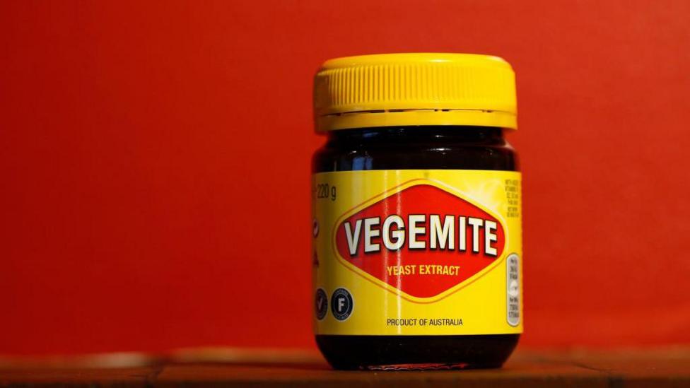 Qizil fonli javonda turgan Vegemite’ning sariq bankasi