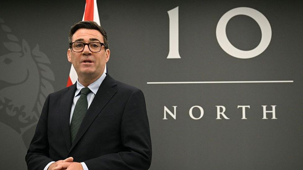 Энди Бёрнем стоит перед вывеской Number 10 North и флагом Великобритании.